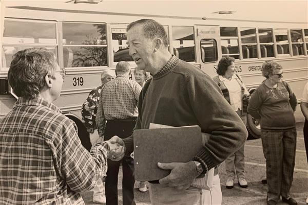 Jack Gaffney shaking hands with a reunion attendee in front of a bus